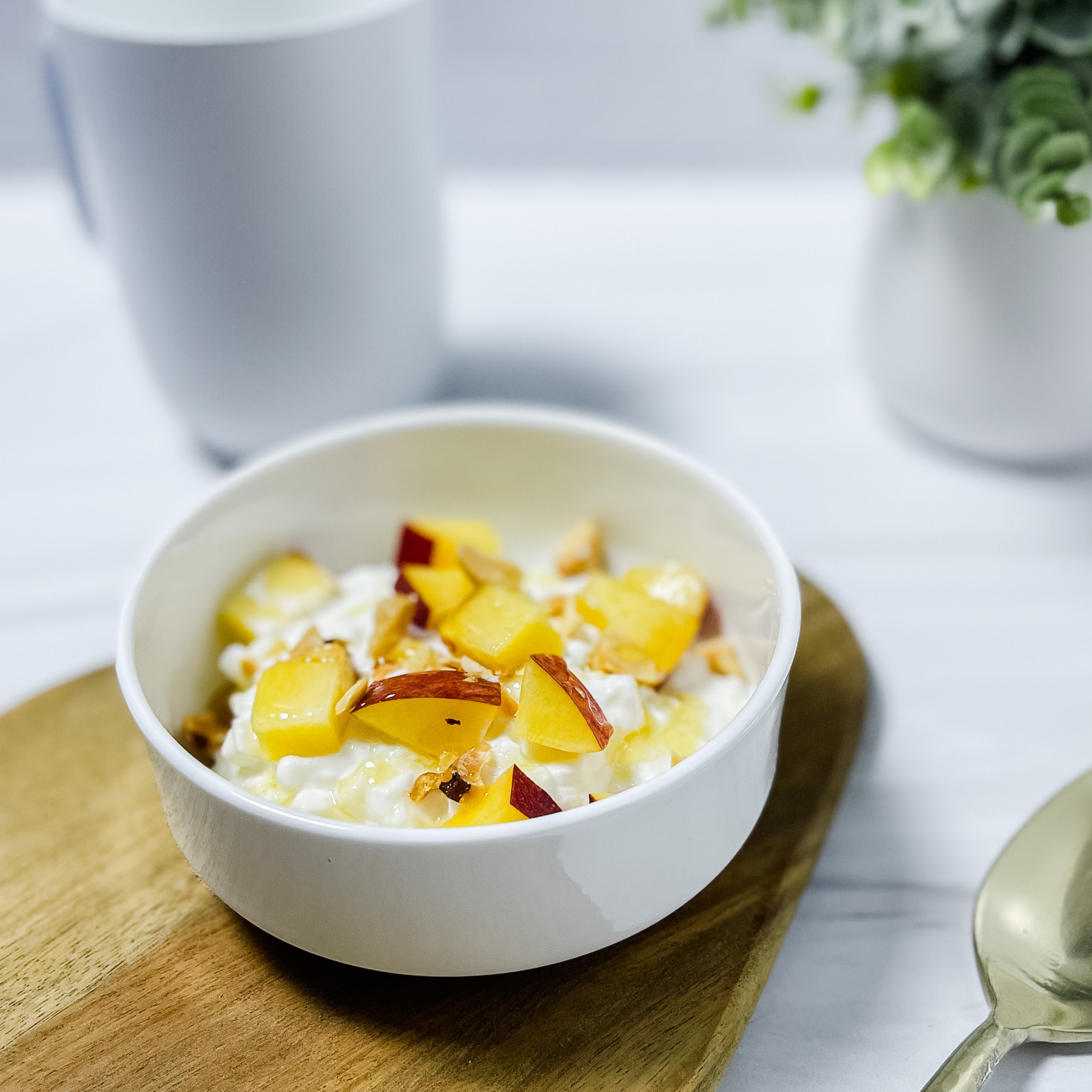 a bowl of cottage cheese topped with peach, brazil nuts and honey atop a wood platter.