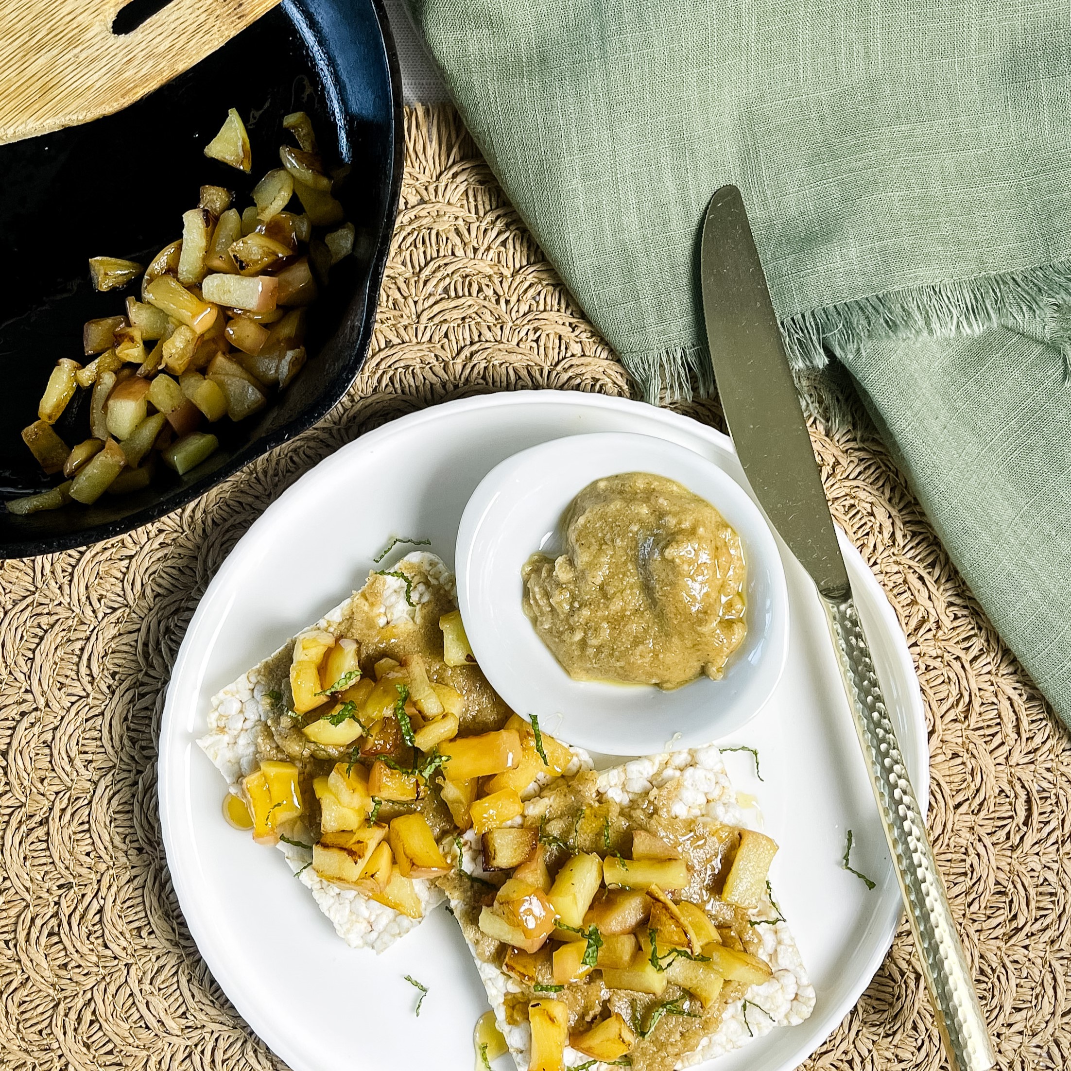 tiger nut butter smeared over a rice cake and topped with warm butter apples and mint. beautifully served on a white plate for a low histamine breakfast